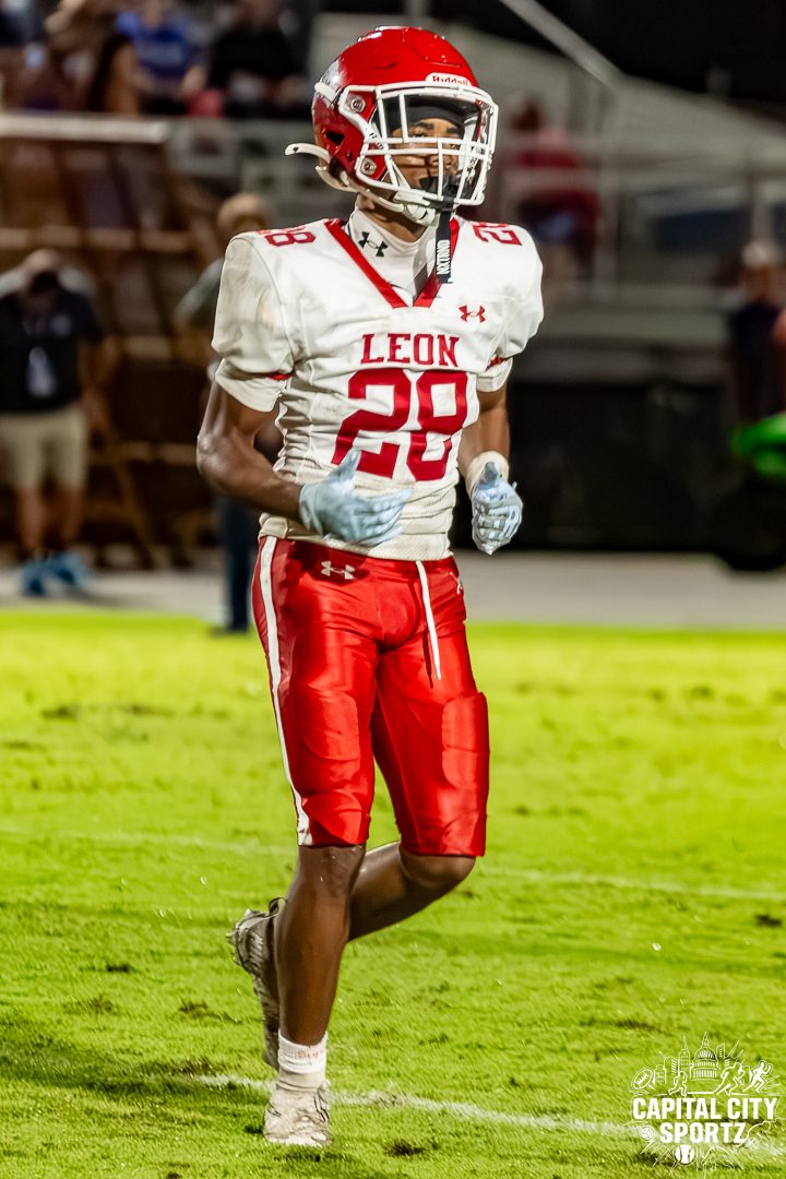 A football player in a red helmet and white number 28 jersey jogs across the field at a night game