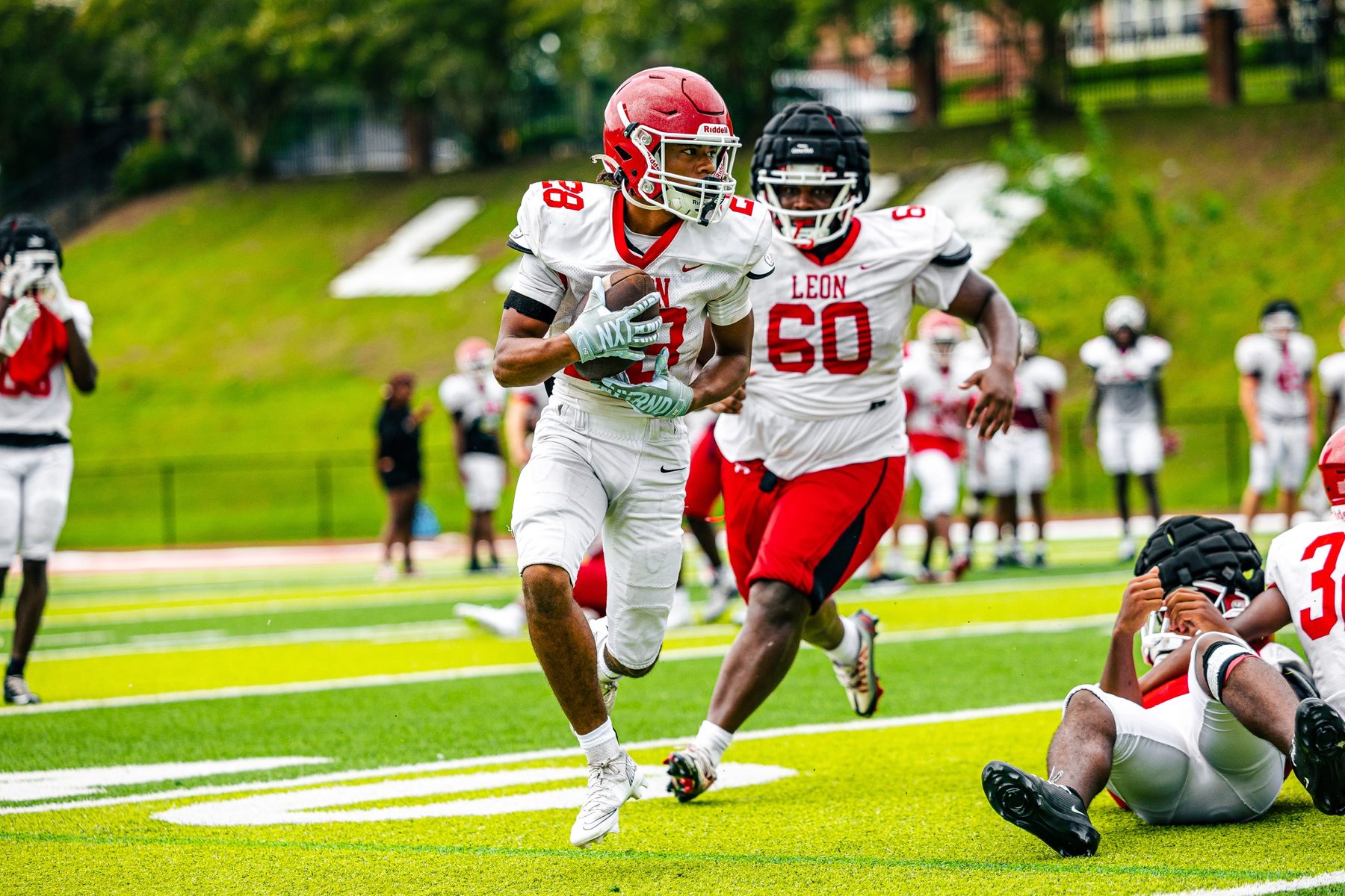 A high school ball carrier in a white and red uniform breaks upfield with a teammate blocking beside him