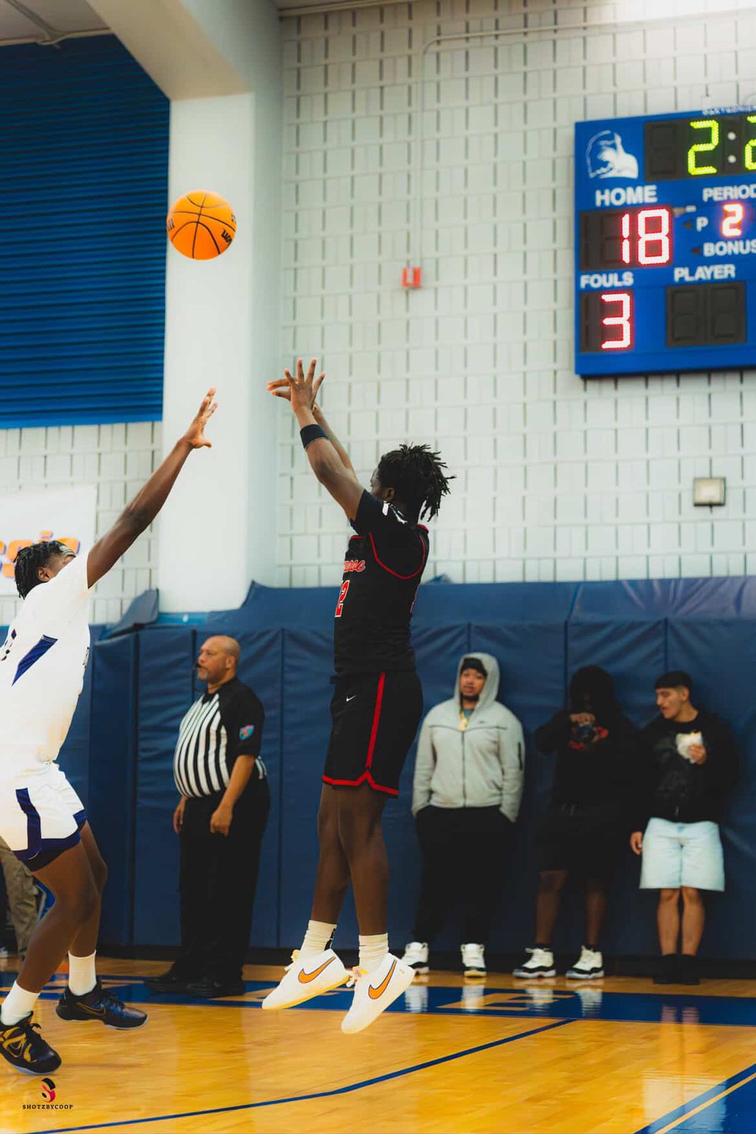 A basketball player in a black uniform releases a jump shot over a defender's outstretched hand